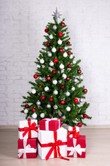 Fototapeta na wymiar christmas tree with colorful balls and gifts over white brick wa
