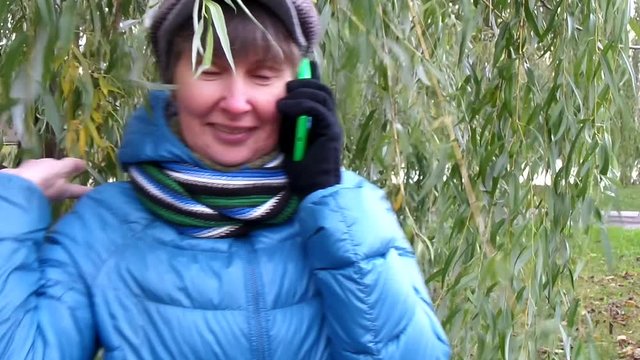 Женшина разговаривает по телефону на фоне ивы осенним вечером/ Телефонный разговор