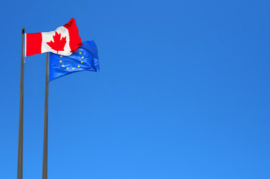 Canadian and European flags waving in the wind over blue sky