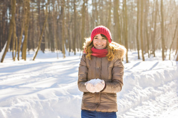 Fototapeta na wymiar Young woman holding natural soft white snow in her hands to make a snowball, smiling during a cold winter day in the forest, outdoors.
