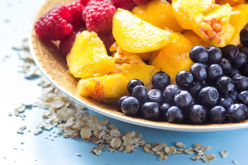 Organic oatmeal porridge in white ceramic bowl with raspberries, peaches and blueberries. Healthy breakfast - health and diet concept on the wooden table, close up.