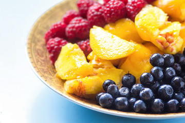 Organic oatmeal porridge in white ceramic bowl with raspberries, peaches and blueberries. Healthy breakfast - health and diet concept on the wooden table, close up.