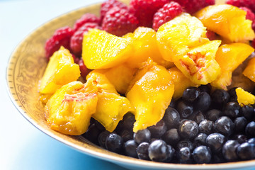 Organic oatmeal porridge in white ceramic bowl with raspberries, peaches and blueberries. Healthy breakfast - health and diet concept on the wooden table, close up.