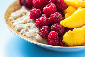 Organic oatmeal porridge in white ceramic bowl with raspberries, peaches and blueberries. Healthy breakfast - health and diet concept on the wooden table, close up.