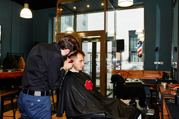 Fototapeta na wymiar Male hairdresser cuts client electric clippers in the barbershop