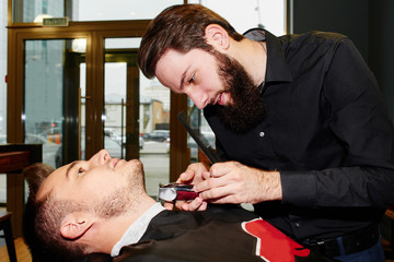 The Barber man in the process of cutting the beard of client electric clippers in the barbershop
