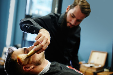 Obraz premium The Barber cleans brush the face of the customer from the hair after a haircut in Barbershop