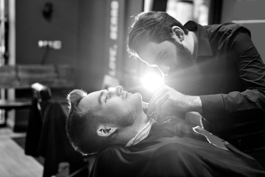 The Barber man in the process of cutting the beard of a client in a Barbershop, black and white photo