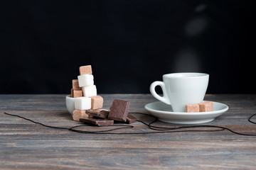 Cup of espresso coffee with sugar cubes and chocolate bars on wooden table.