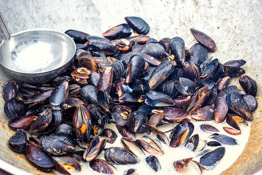 Steamed mussels in white wine sauce cooking at large metallic pan. Fresh mussels at grill pan. Seafood barbecue outdoors. Picnic healthy food, mussels in shells. Stewed clams, mediterranean cuisine.