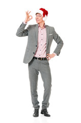 Caucasian businessman wearing christmas hat for santa. Young man in suit doing a ok gesture and looking at camera. Full body picture of a happy modern Santa Claus.