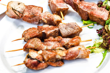 Grilled meat kebabs on the white plate. Skewered on wooden sticks tasty pork meat. Shashlik or Shish kabab.