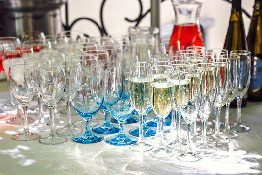 Beautiful row line of different glasses filled with champagne are lined up ready to be served on a christmas party, martini, vodka,and others on decorated catering bouquet table on open air event.