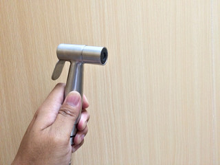 Hand using a bidet shower on wooden wall in toilet(restroom)