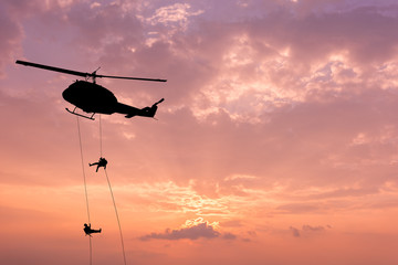 Silhouette of helicopter, soldiers rescue helicopter operations on sunset sky background.