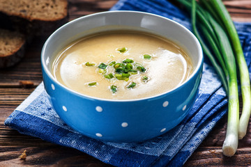 Homemade vichyssoise cream soup served with chives, in blue bowl on wooden table. Potato and Leek Soup.