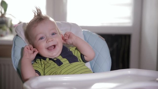 Cute shy baby in a baby chair laughing and looking into camera. HD.