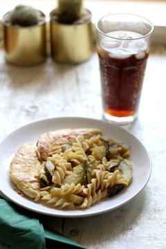 Chicken breasts, pasta and zucchini with melted cheese. Soda with ice in a tall glass. Selective focus.
