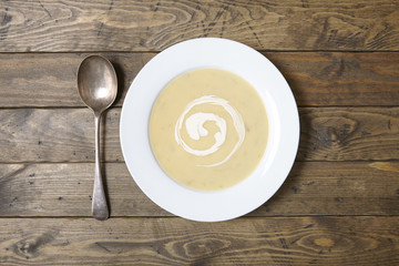 Aerial view of a bowl of hot chicken soup with swirl of cream on a rustic dinner table background