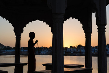 Silhouette of a sadhu performing ritual prayer in the evening at Pushkar Lake. One of the holiest...