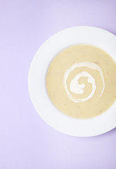 A bowl of hot chicken soup with swirl of cream on a pastel purple background