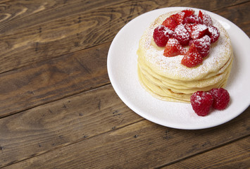 A stack of berry covered pancakes on a wooden table background with blank space at side