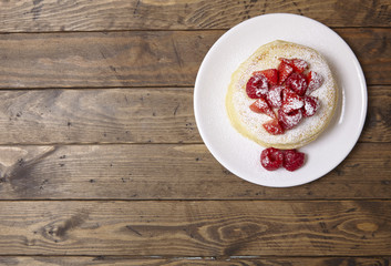 Aerial view of a stack of berry covered pancakes on a wooden table background with blank space at side