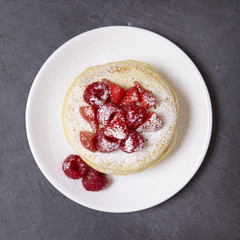 A stack of berry covered pancakes on a rustic slate background