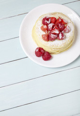 A stack of berry covered pancakes on a blue wooden table background with blank space below
