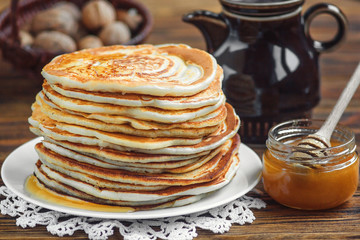 Stack of delicious, homemade pancakes with honey on white plate on wooden background. Healthy breakfast, close up.