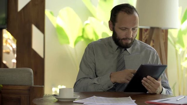 Young businessman comparing data on tablet and smartphone by table at home
