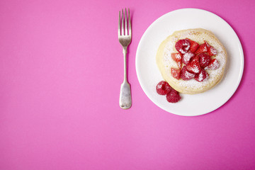 Aerial view of a stack of berry covered pancakes on a bright pink background with blank space along side