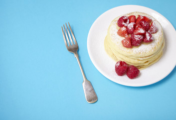 A stack of berry covered pancakes on a bright blue background with fork and blank space at side