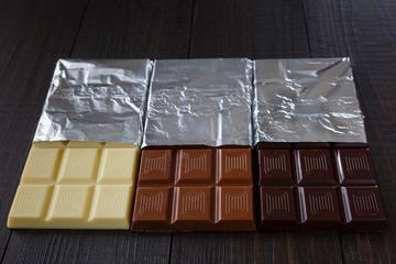 White, milk, black chocolates in foil on dark wooden boards