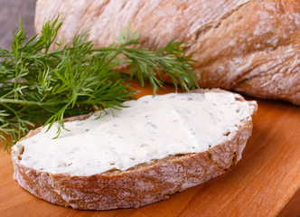 A slice of freshly baked ciabatta bread and healthy low fat cream cheese with dill and fresh green dill on wooden board.