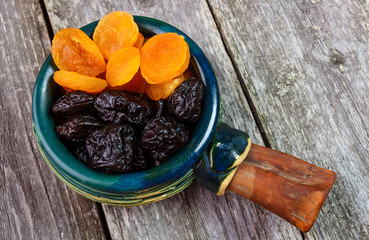 Organic prunes, dried plums and dried apricots in old tableware on rustic table. Top view