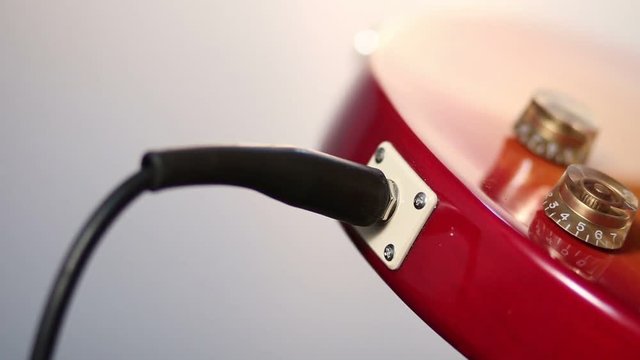 Plugging in cord into jack of electric guitar.