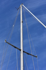Metal oval profile yacht mast with cordage.