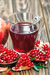 glass of pomegranate juice with ripe fresh punica granatum fruits with leaves on wooden table close-up