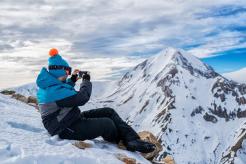 Fototapeta na wymiar Man in ski suit taking photos of mountain landscape with smartphone.