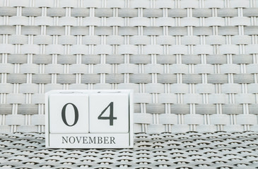 Closeup surface white wooden calendar with black 4 november word on blurred weave wood chair...