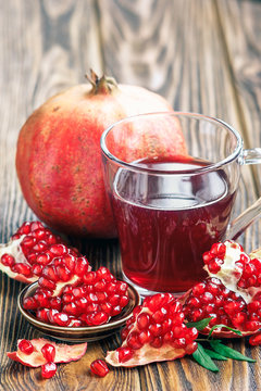 glass of pomegranate juice with ripe fresh punica granatum fruits with leaves on wooden table close-up