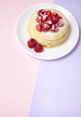 A stack of fruit covered pancakes on a pastel pink and purple background forming a page header