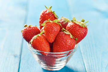 Strawberries in glass bowl on blue wooden table