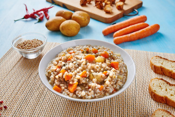 Buckwheat soup in white bowl surrounded by ingredients on wooden blue table