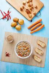 Buckwheat soup in white bowl surrounded by ingredients on wooden blue table