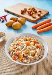 Buckwheat soup in white bowl surrounded by ingredients on wooden blue table