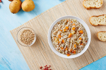 Buckwheat soup in white bowl surrounded by ingredients on wooden blue table