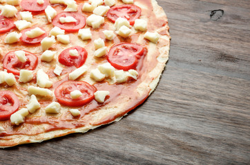Raw pizza dough with cheese and tomatoes on wood table