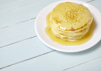 A stack of golden syrup covered pancakes on a wooden table background